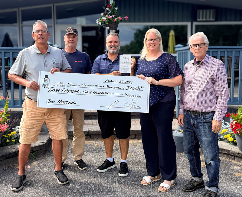 Fred Drodge and volunteers presenting a donation cheque outside a community building