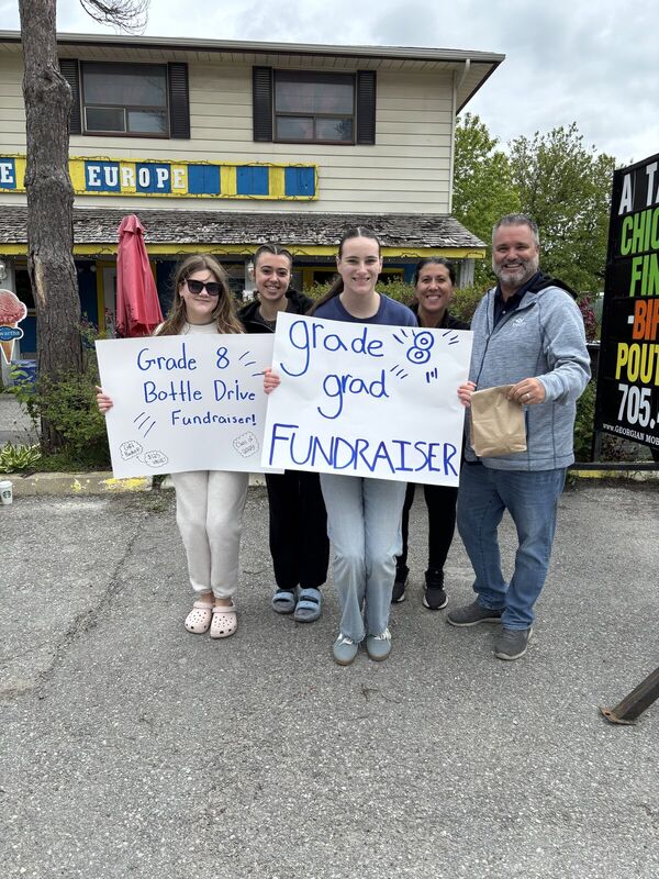 Students holding Grade 8 bottle drive fundraiser signs with Fred Drodge