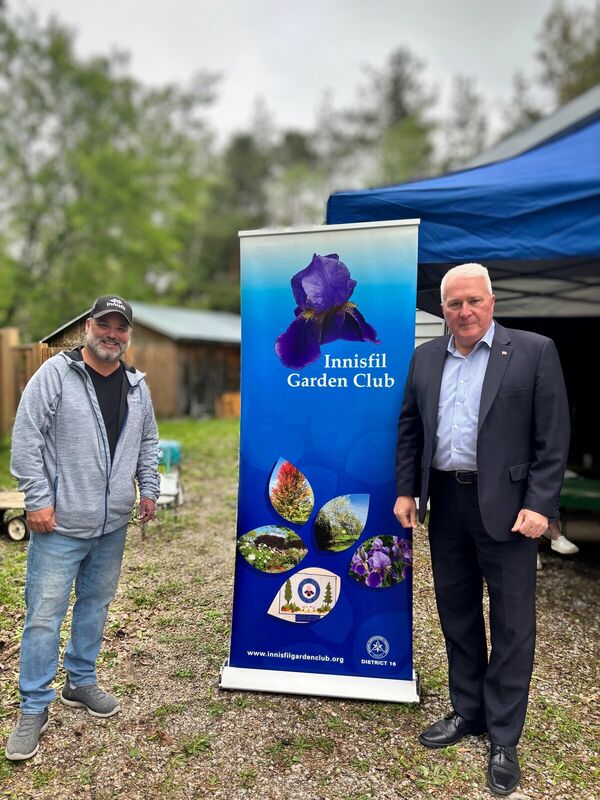 Fred Drodge in a suit beside an Innisfil Garden Club banner